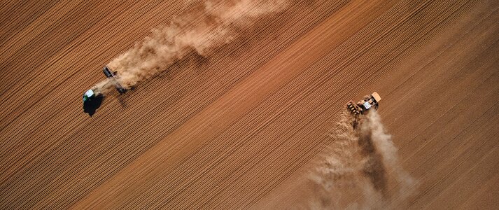 Na zdjęciu znajduje się widok na pola z lotu ptaka, orane przez dwa traktory.