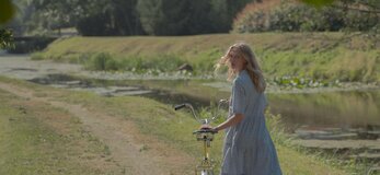 Zdjęcie przedstawia dziewczynę z rowerem w wiejskiej scenerii