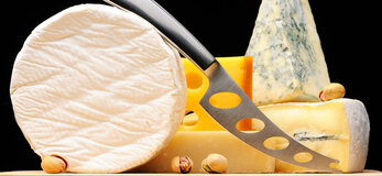 Na zdjęciu znajdują się różne sery na desce do krojenia, z nożem do krojenia sera na pierwszym planie.
