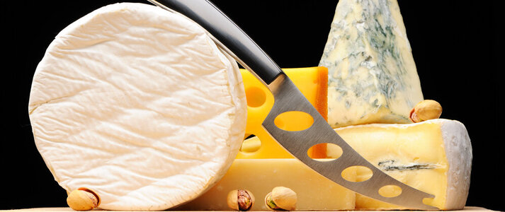 Na zdjęciu znajdują się różne sery na desce do krojenia, z nożem do krojenia sera na pierwszym planie.