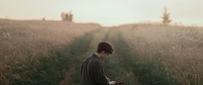 Na zdjęciu znajduje się mężczyzna siedzący na polnej drodze, wpatrzony w książkę.