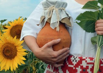 Zdjęcie przedstawia kobietę na polu słoneczników, trzymającą w ręce wazon gliniany.