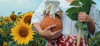 Zdjęcie przedstawia kobietę na polu słoneczników, trzymającą w ręce wazon gliniany.