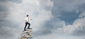 Zdjęcie przedstawia osobę wspinającą się po książkach w stronę prawą kadru.