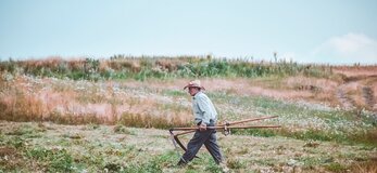 Zdjęcie przedstawia starszego rolnika idącego po polu.
