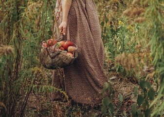 Na zdjęciu jest kobieta trzymająca kosz z płodami rolnymi.