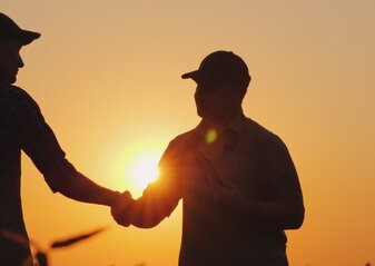 Zdjęcie przedstawia dwóch rolników podających sobie rękę na polu, o zachodzie słońca.