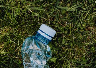 Na zdjęciu widać butelkę plastikową rzuconą na trawnik.