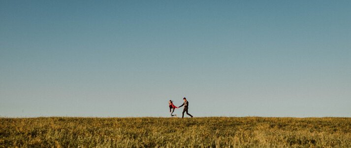 Zdjęcie przedstawia parę biegnącą po polu, trzymającą się za ręce wokół wiejskiego krajobrazu.