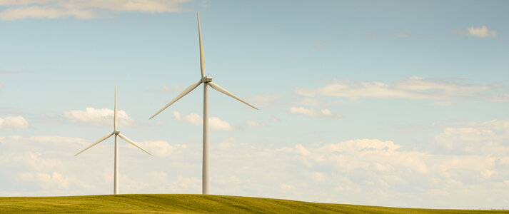 Zdjęcie przedstawia turbiny wiatrowe w pustym krajobrazie wiejskim, w polu łączącym się na horyzoncie z niebem leniwie.