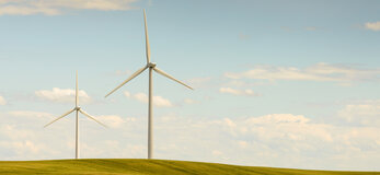 Zdjęcie przedstawia turbiny wiatrowe w pustym krajobrazie wiejskim, w polu łączącym się na horyzoncie z niebem leniwie.